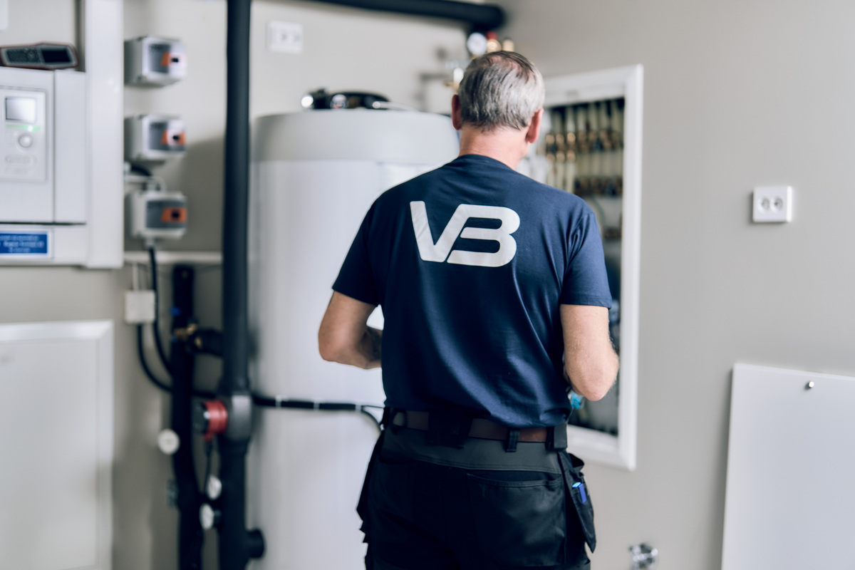 VB-rørlegger i blå t-skjorte på jobb i teknisk rom med varmtvannsbereder og vannsikringsskap.